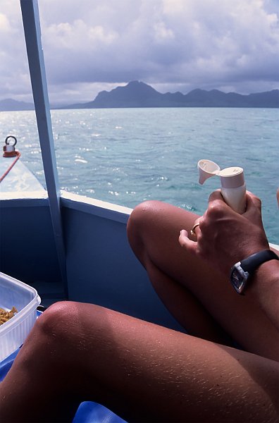 Sunbather on boat applying sun lotion, against an Indian Ocean island background